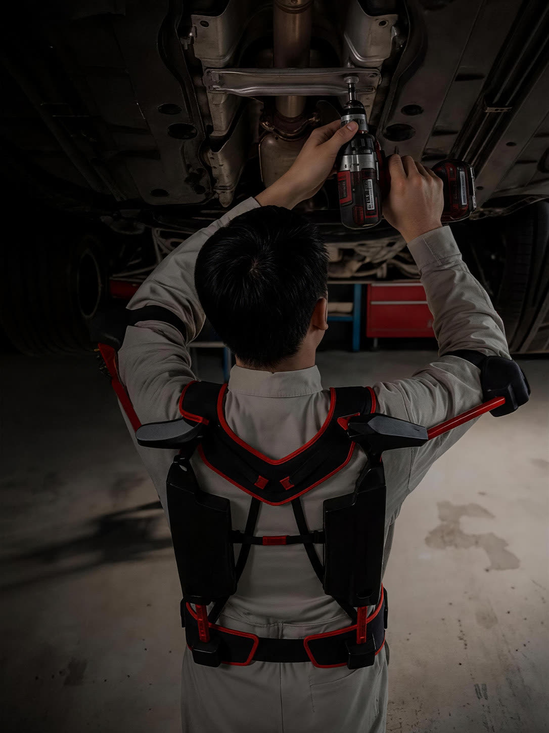 Technician working overhead under a vehicle wearing an arm support exoskeleton